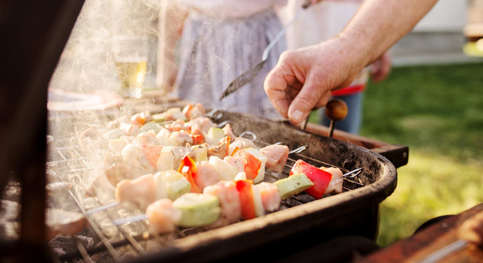 A person cooking skewered food on a BBQ
