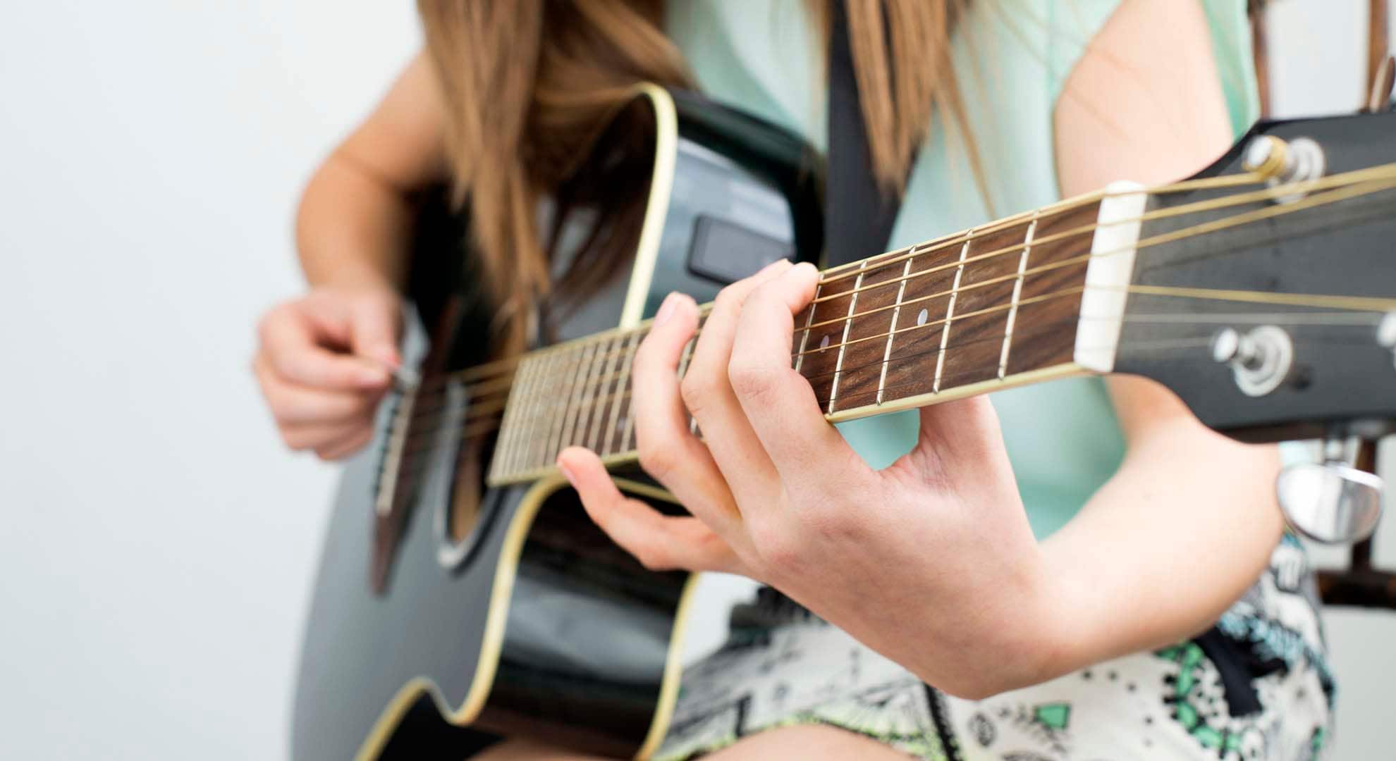 Photo of a girl learning to play chords on a guitar