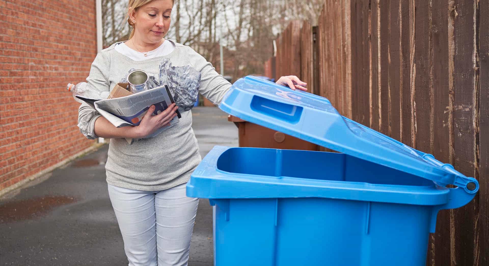 Photo of a person putting recycling in a blue wheelie bin