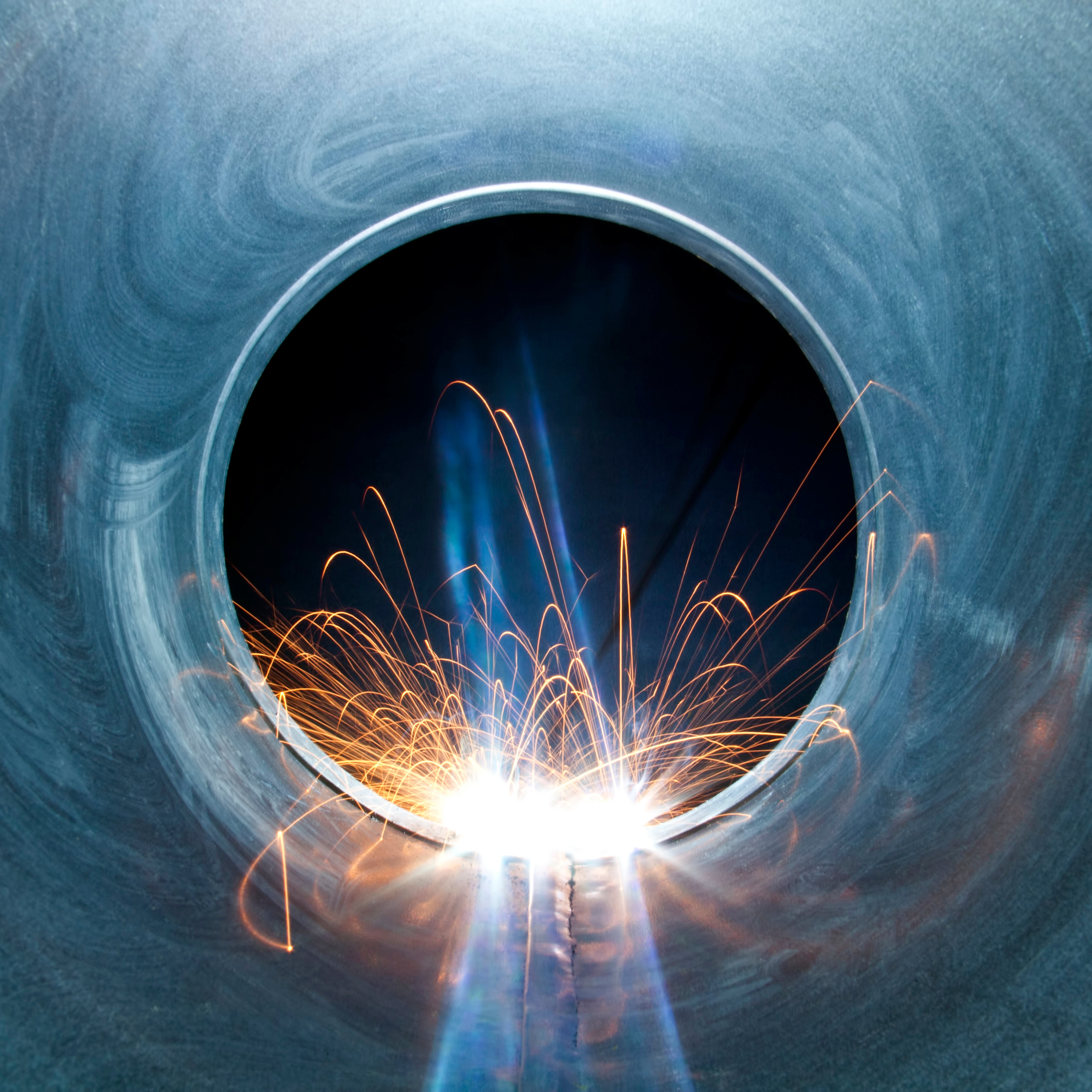 The interior of a metal pipe showing the circular exit. The pipe is being welded with sparks flying inside.